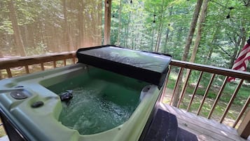 A hot tub on a wooden deck with a view of a forest.