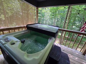 A hot tub on a wooden deck with a view of a forest. - Owl's Tale at Avenwood Cabins (New Straitsville)
