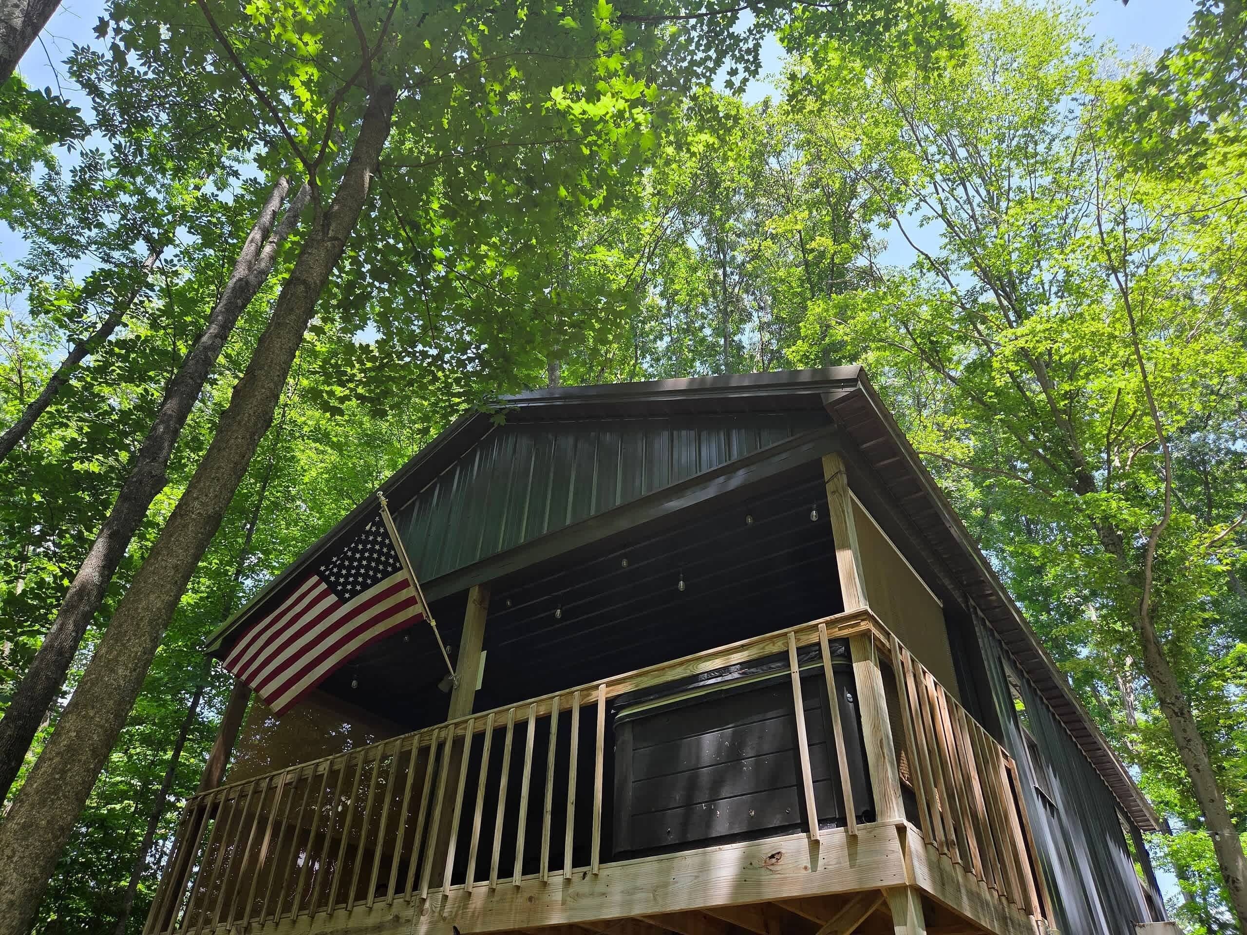 Een houten hut met een balkon en een Amerikaanse vlag, omgeven door bomen.