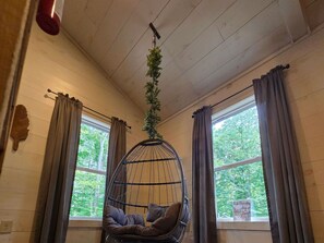 A room with a hanging chair, large windows, and curtains. - Owl's Tale at Avenwood Cabins (New Straitsville)