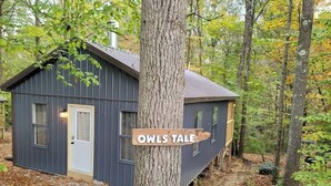 Une petite cabane, dans un endroit boisé, sur laquelle est accrochée une pancarte indiquant « OWLS TALE  ».