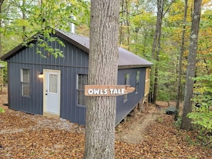 Une petite cabane, dans un endroit boisé, sur laquelle est accrochée une pancarte indiquant « OWLS TALE ».