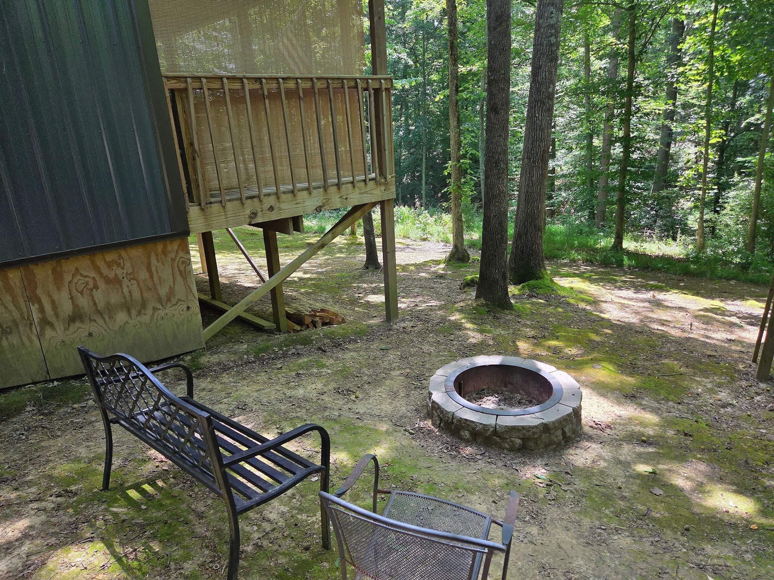 A wooden deck with a bench and a fire pit in a forested area.