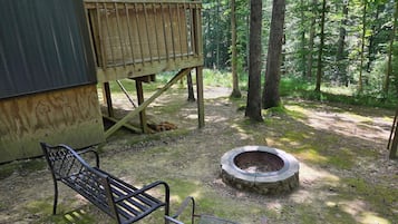 A wooden deck with a bench and a fire pit in a forested area.