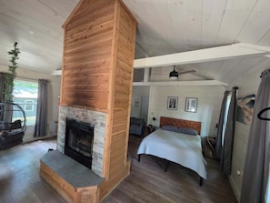 Une pièce avec une cheminée, un lit, un fauteuil suspendu et un ventilateur de plafond.