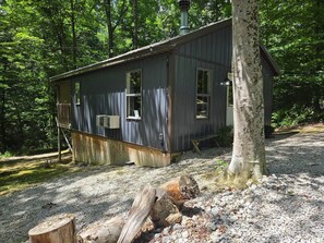 A rustic cabin with a wooden deck, a chimney, and a gravel ground. - Owl's Tale at Avenwood Cabins (New Straitsville)