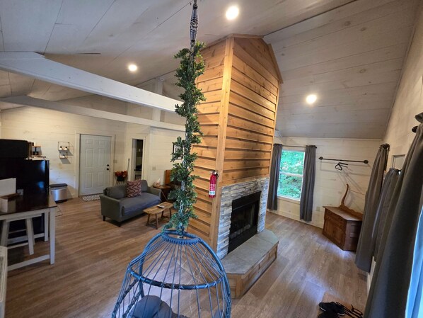A spacious living area with a stone fireplace, wooden walls, and a hanging plant.