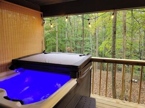 Ein Whirlpool auf einer Holzterrasse mit Blick auf einen Wald.