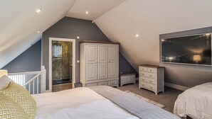 Een slaapkamer met een schuine kap, een bed, een kledingkast, een dressoir en een aan de muur bevestigde televisie.