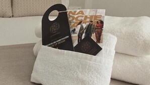 A white towel on a bed with a black tag holder containing a magazine.