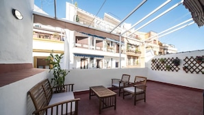 A rooftop patio with wooden furniture, a potted plant, and a lattice wall with hanging plants.