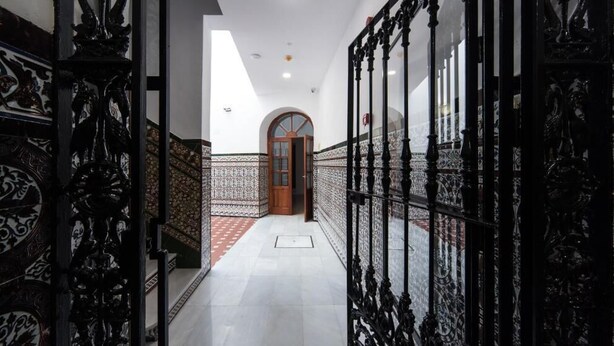 A corridor with ornate black metal railings, a tiled floor, and a wooden door at the end.