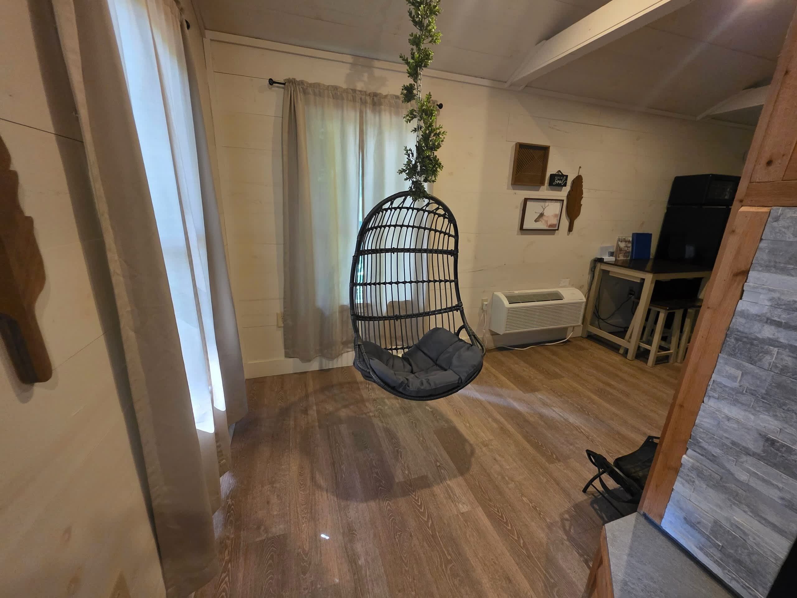 A room with a hanging chair, a radiator, a television, and a wooden floor.
