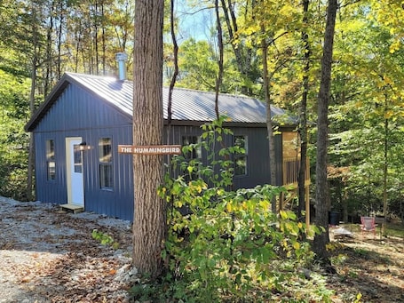 A small cabin labeled 'The Hummingbird' surrounded by trees.. Hummingbird at Avenwood Cabins