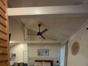 A room with a ceiling fan, a bed with a headboard, two framed pictures on the wall, and a window with curtains.