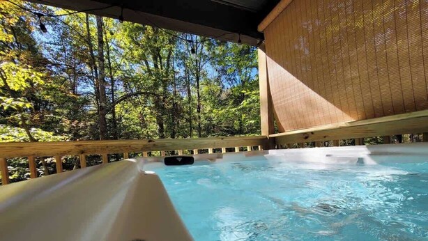 A hot tub with a wooden deck and a view of a forest. - Hummingbird at Avenwood Cabins (New Straitsville)