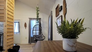 A modern interior with a wooden dining table, a hanging plant, a black chair, and a wooden wall. - Hummingbird at Avenwood Cabins (New Straitsville)