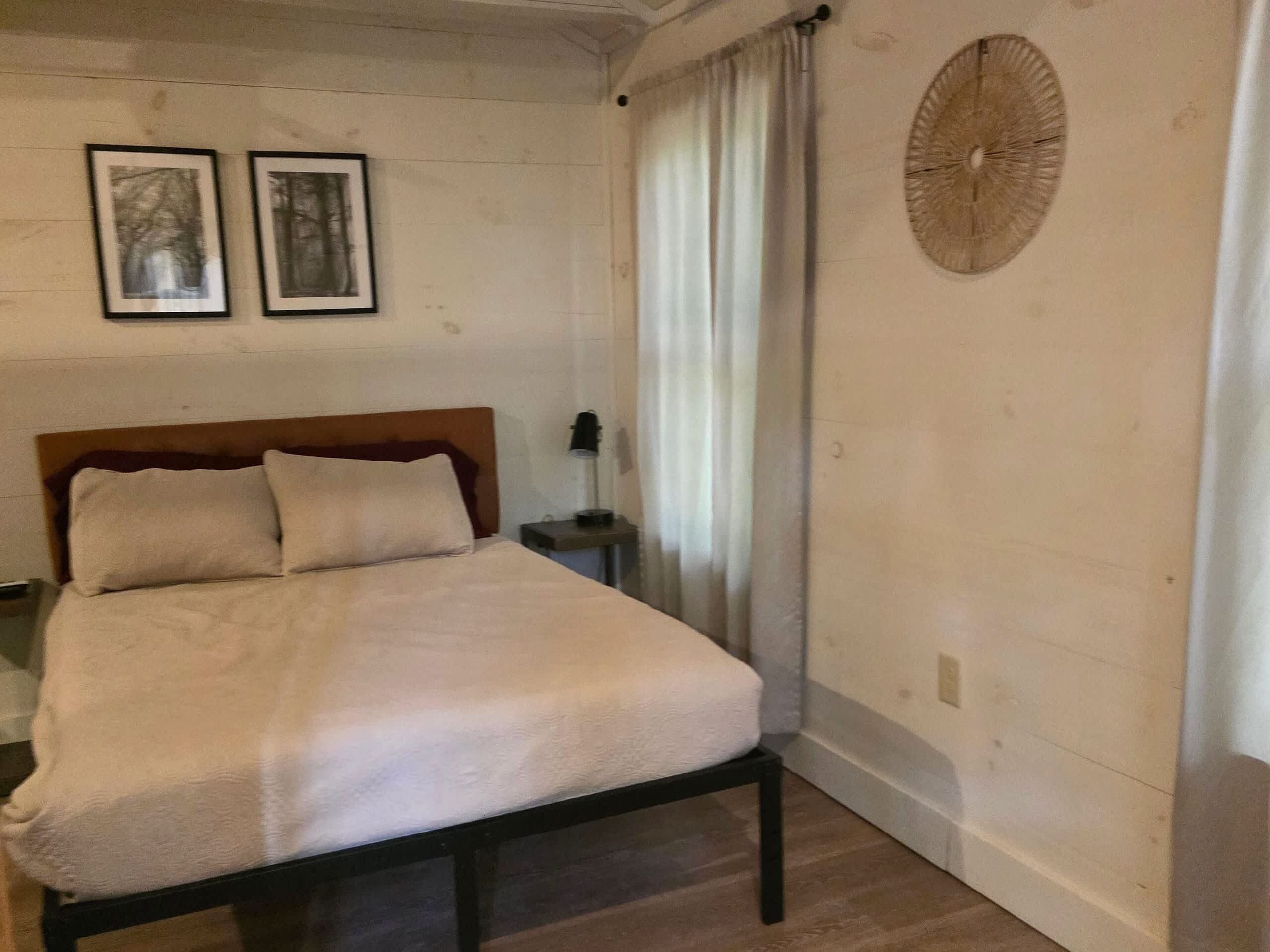 A bedroom with a bed, a nightstand, a lamp, and two framed pictures on the wall.