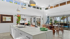 Une cuisine spacieuse dotée d’un grand îlot central, d’un éclairage moderne suspendu et offrant une vue sur l’extérieur.