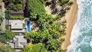 Vue aérienne d’une propriété située sur la côte, avec une piscine, plusieurs maisons et une plage.