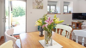 A dining area with a wooden table, chairs, and a vase with flowers. - Old Highwood - Piglet Cottage (Dunkeswell)