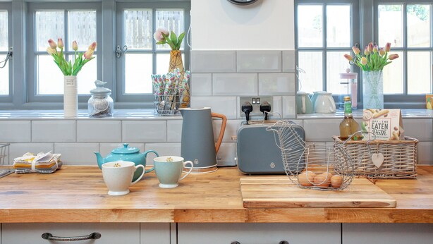 A kitchen with a wooden countertop, a kettle, teapots, a toaster, a basket with eggs, and tulips in vases. - Old Highwood - Piglet Cottage (Dunkeswell)