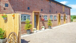 A brick building with multiple doors and windows, a wooden fence, and potted plants. - Old Highwood - Piglet Cottage (Dunkeswell)