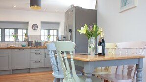 A dining area with a wooden table, chairs, and a bottle of champagne. - Old Highwood - Piglet Cottage (Dunkeswell)