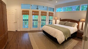 Un dormitorio con una cama grande, suelo de madera, vista a través de puertas francesas y una mesita de noche con lámpara.
