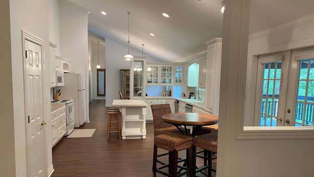 Una cocina moderna con armarios blancos, una mesa de comedor de madera y vistas al exterior a través de amplios ventanales.