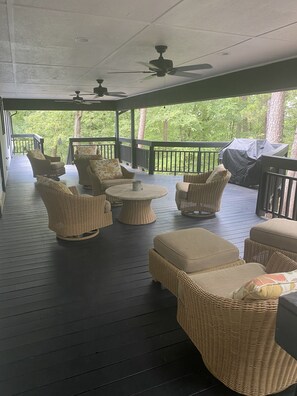 A covered outdoor seating area with wicker furniture, ceiling fans, and a barbecue grill.