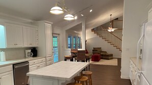 Una cocina amplia con una isla grande, taburetes de bar de madera y una escalera que conduce a una zona de altillo.