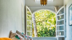 Um quarto com uma cama, uma janela com uma persiana aberta, uma mesa de cabeceira branca e chão de tijolos.