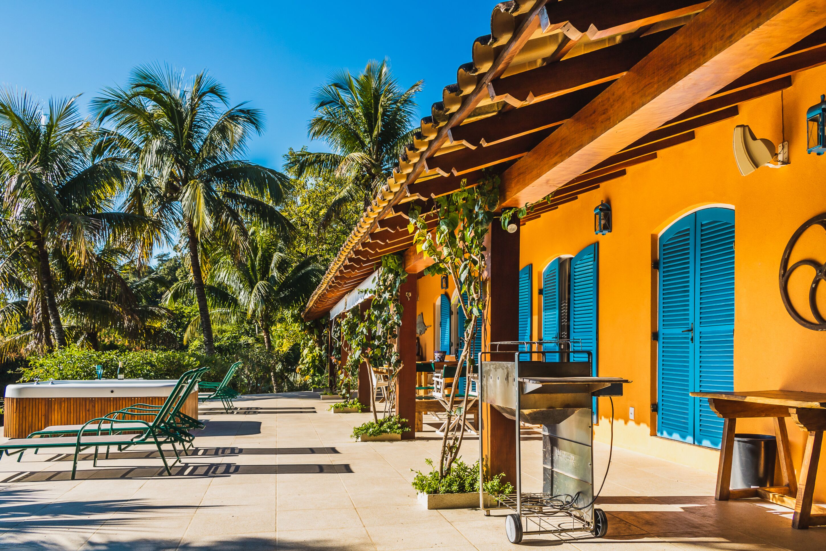 A tropical resort with outdoor seating, palm trees, and a bright yellow building with blue shutters.