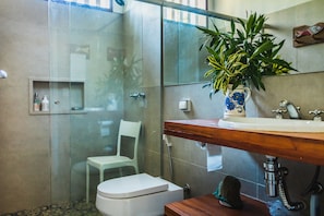 Ein modernes Badezimmer mit einer gläsernen Duschkabine, einer weißen Toilette, einem hölzernen Waschtisch mit Waschbecken und einer Topfpflanze.