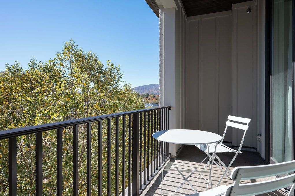 A balcony with a white table and chairs, a black railing, and a view of trees and hills.