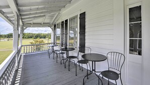 A covered porch with a white exterior, featuring a series of black metal tables and chairs, and a view of a green landscape. - Stunning historic home w/ large rooms. Close to attractions. Kid & pet friendly! (Sellers)