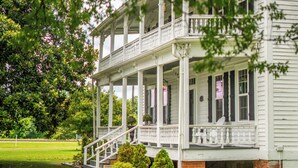 A two-story house with a porch, brick foundation, and a small garden. - Stunning historic home w/ large rooms. Close to attractions. Kid & pet friendly! (Sellers)