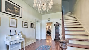 A hallway with a white desk, framed pictures on the wall, a chandelier, and a staircase. - Stunning historic home w/ large rooms. Close to attractions. Kid & pet friendly! (Sellers)