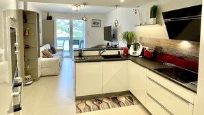 A modern kitchen with white cabinets, a black countertop, and a red stove. There is a dining area with a white table and chairs, and a sliding glass door leading to a balcony. - Le discret - Plage de Foncillon 4* (in French) (Royan)