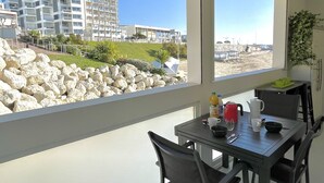 A dining area with a table and chairs, a view of a beach, and a building in the background. - Le discret - Plage de Foncillon 4* (in French) (Royan)