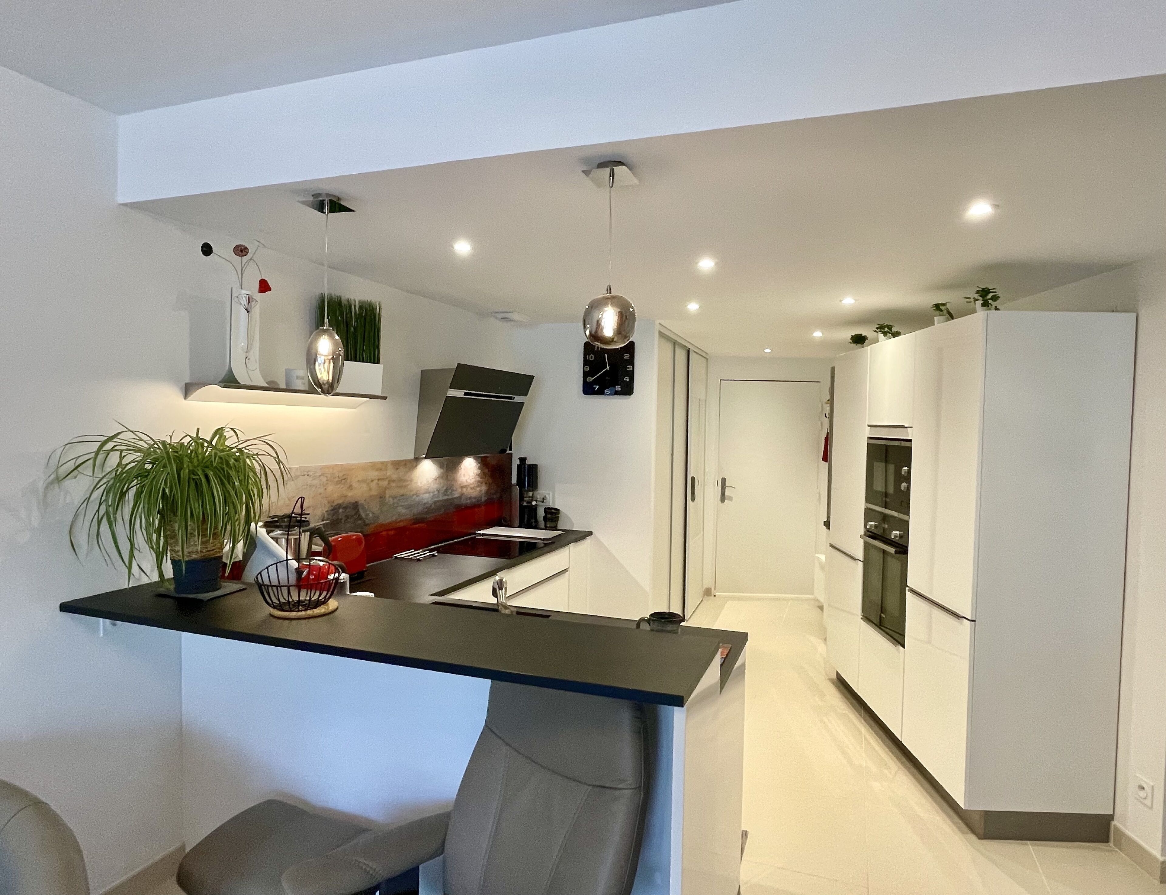 A modern kitchen with a central island, a dining area with two chairs, and a refrigerator.