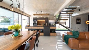 Una cocina moderna con una isla central, un comedor con mesa de madera y sillas de cuero, y una escalera que conduce a un nivel superior.