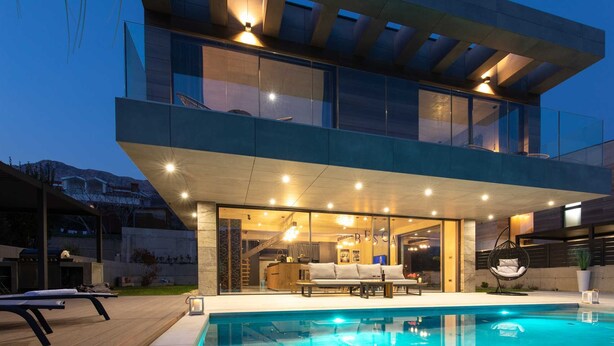 Una casa moderna de dos pisos con piscina, mobiliario exterior y un interior bien iluminado.