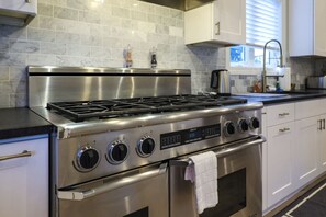 Enjoy cooking in this well-equipped kitchen with a stainless steel range and oven, digital clock display, and white cabinetry.