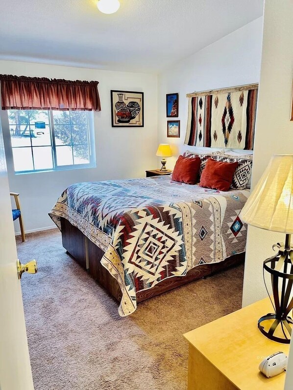 A bedroom with a bed, a window, a nightstand, a lamp, and a door.