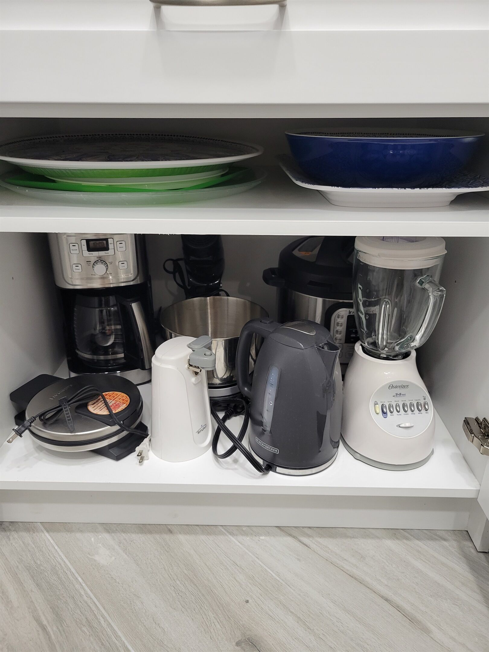Una cocina con cafetera, hervidor, licuadora y plancha para gofres sobre la encimera.