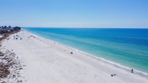 Una playa extensa con agua azul cristalina, algunas personas y unas sillas de playa.