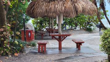 Zona de pati amb una sobreada de palla, bancs de fusta i una barbacoa.