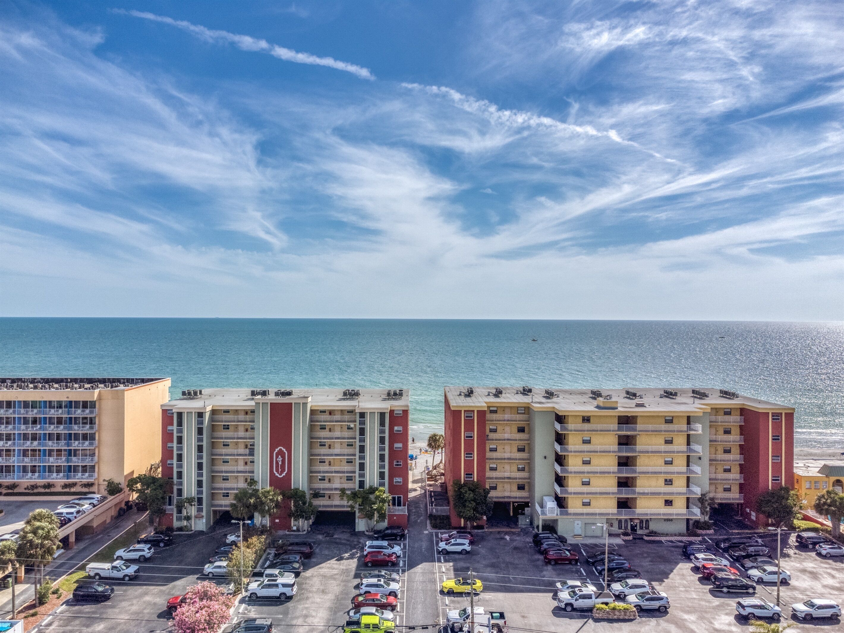 A multi-story parking lot with several cars, a building with a red and yellow facade, and a view of the ocean.